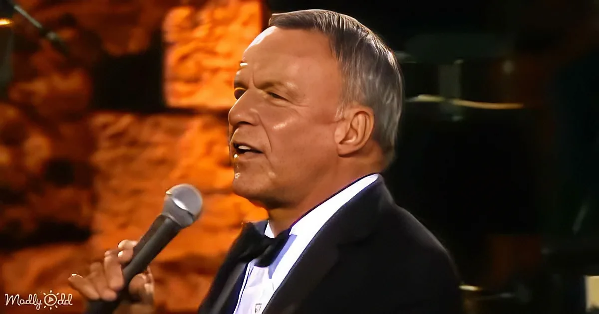A man in a suit sings into a microphone, holding it with his right hand.