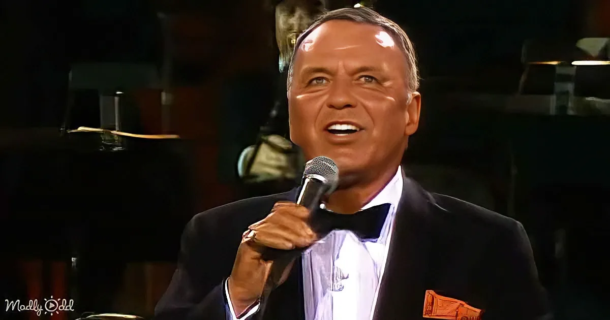 A man in a tuxedo sings into a microphone, holding it with one hand.