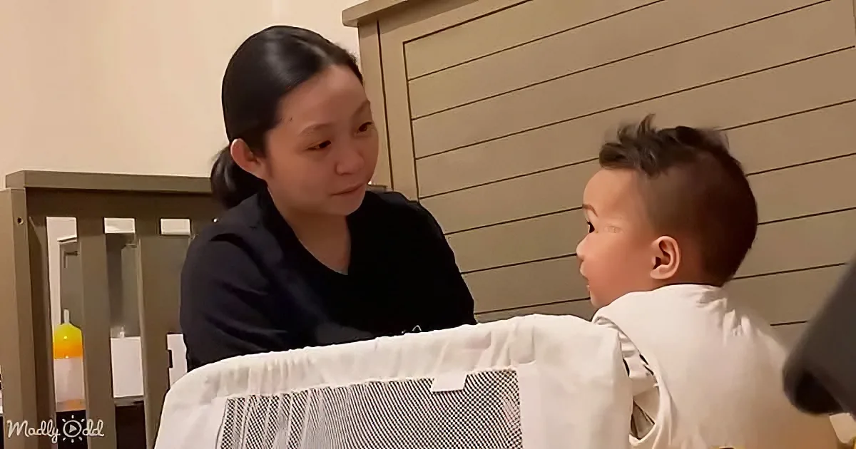 A woman in a black shirt interacts with a young child in a white shirt, both seated indoors.