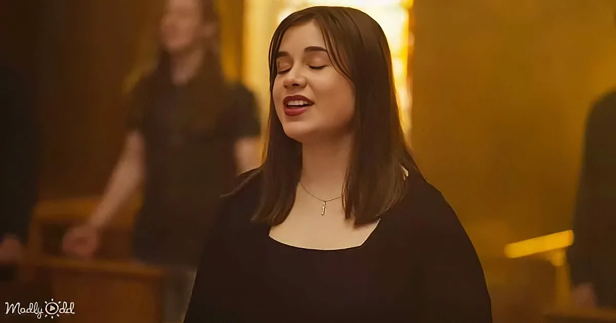 A woman with long dark hair and a black top sings passionately in a warmly lit room.