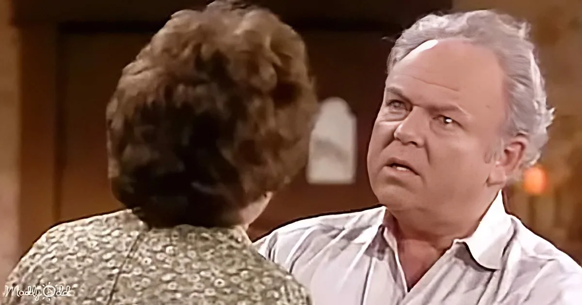 An older man in a striped shirt looks concerned while talking to a woman with short brown hair.