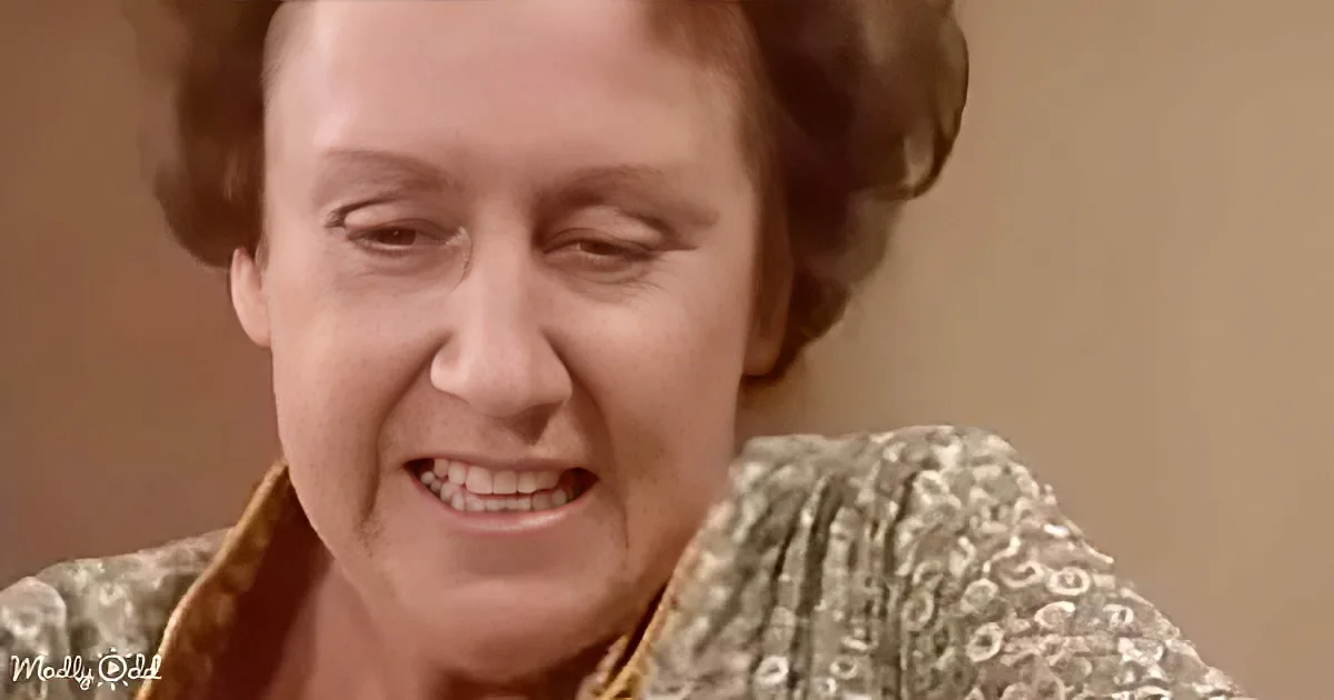 A woman with short, dark hair, wearing a patterned top, smiles warmly, looking downward.