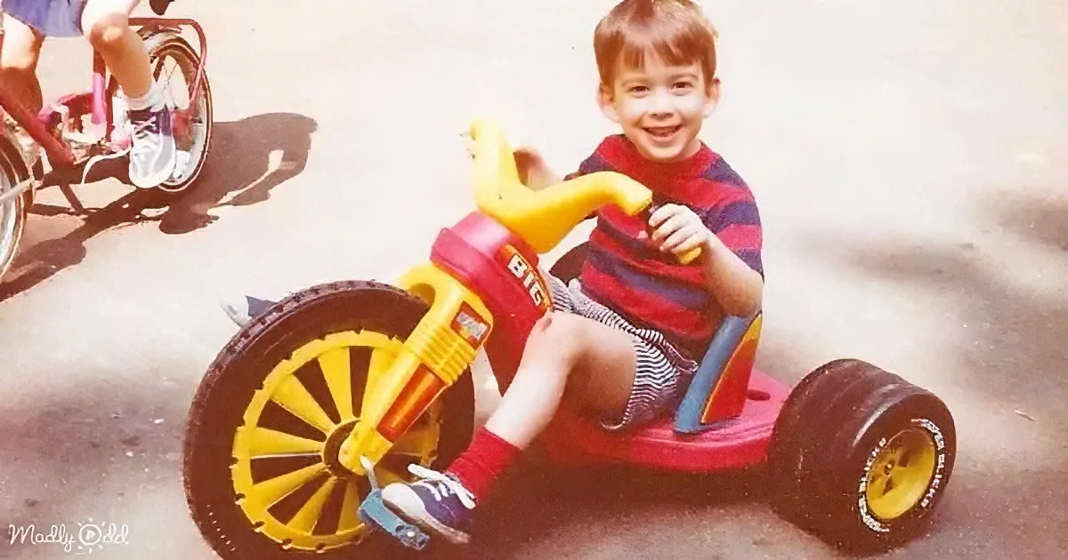 A young boy smiles while riding a red and yellow toy car with large wheels.