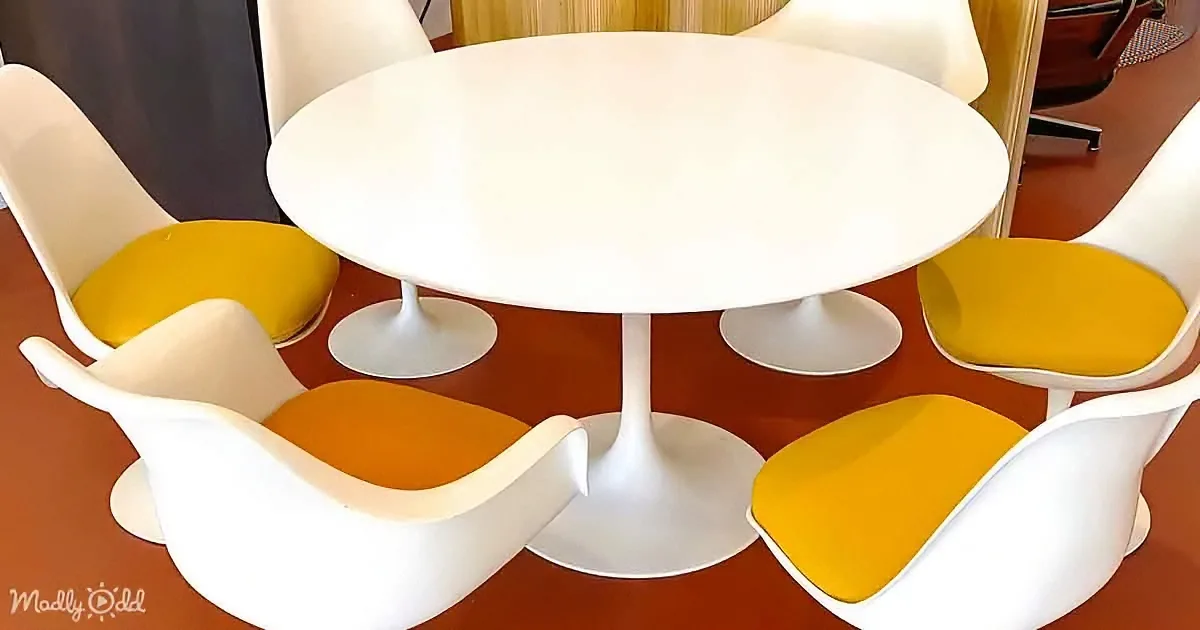 A modern white tulip table surrounded by six white and yellow chairs on a red floor.