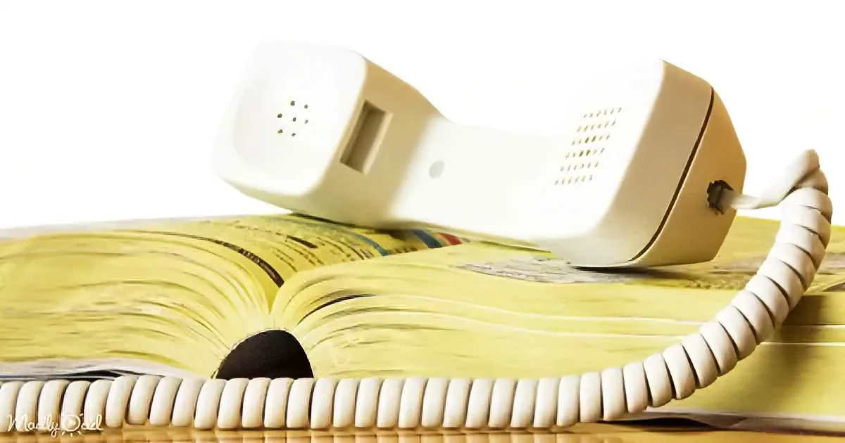 A white rotary phone rests on an open book with a coiled cord.