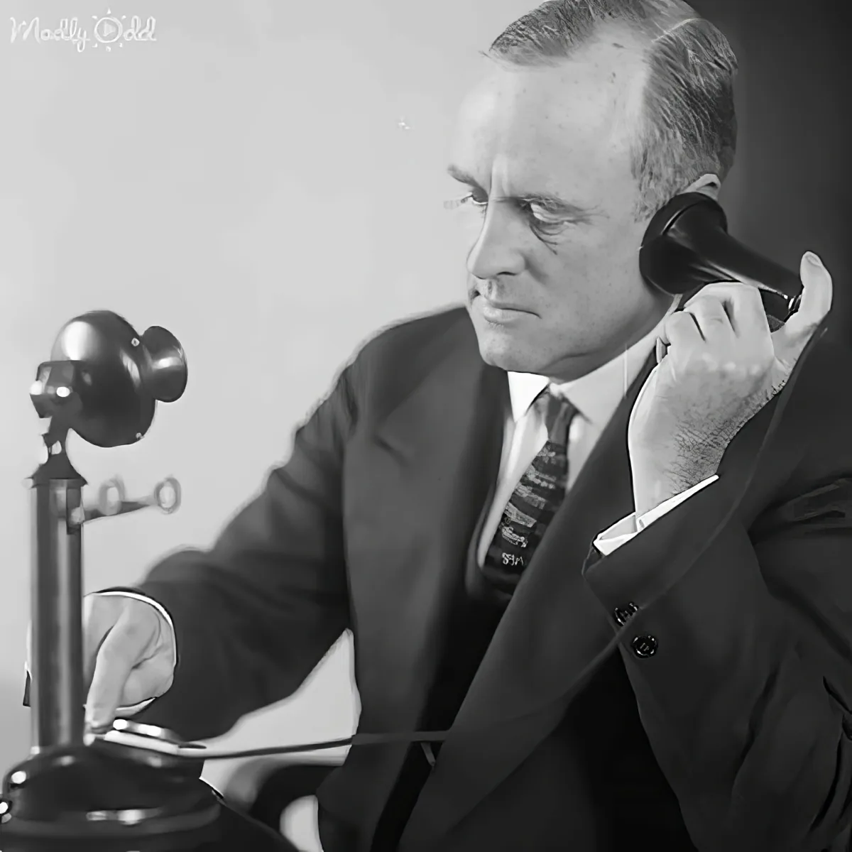 A man in a suit and tie is talking on a vintage telephone, appearing focused.