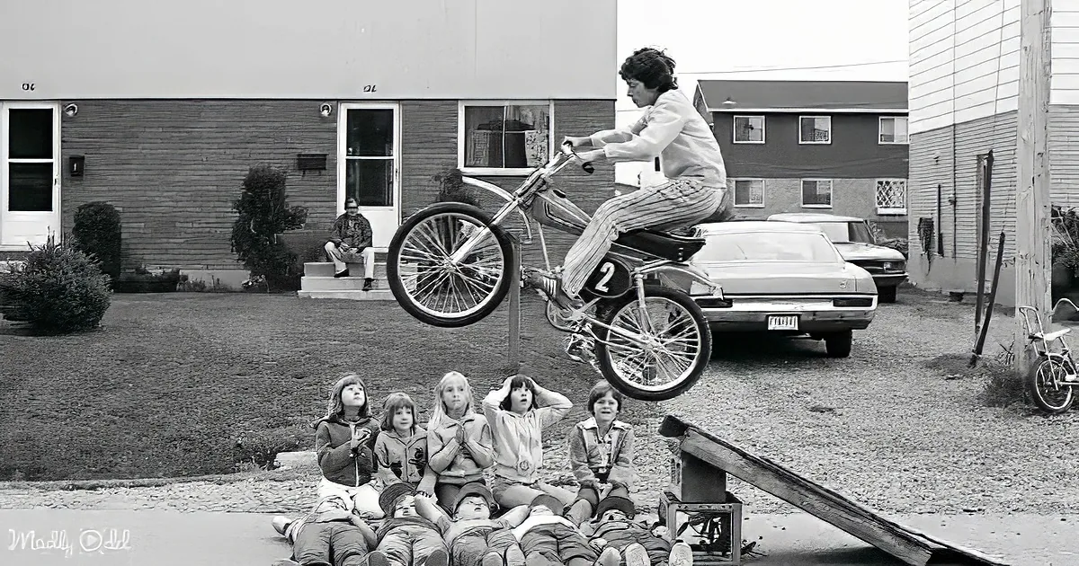 A person rides a BMX bike over a group of children in a suburban setting.