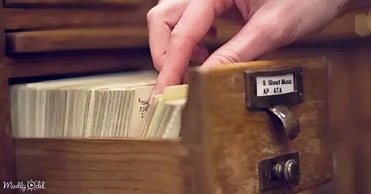 A hand reaches into a wooden filing cabinet drawer, pulling out a file.