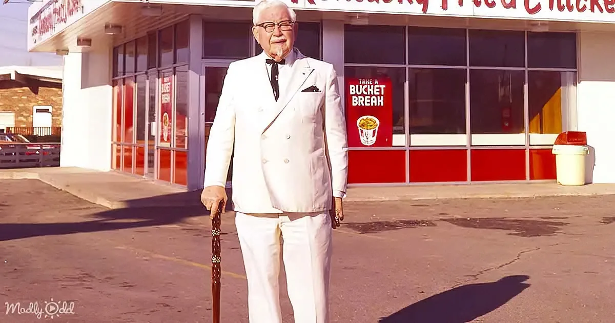 A man in a white suit holds a cane, standing in front of a KFC restaurant.