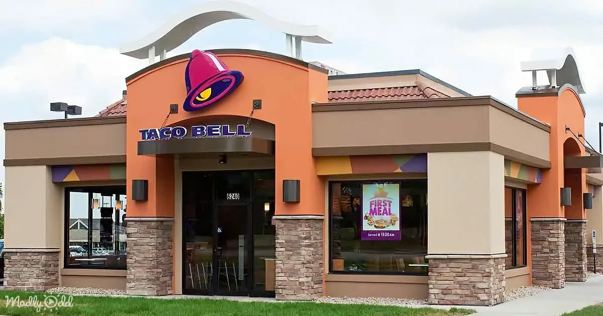 A Taco Bell restaurant with a colorful facade, large bell logo, and a "First Meal" sign in the window.