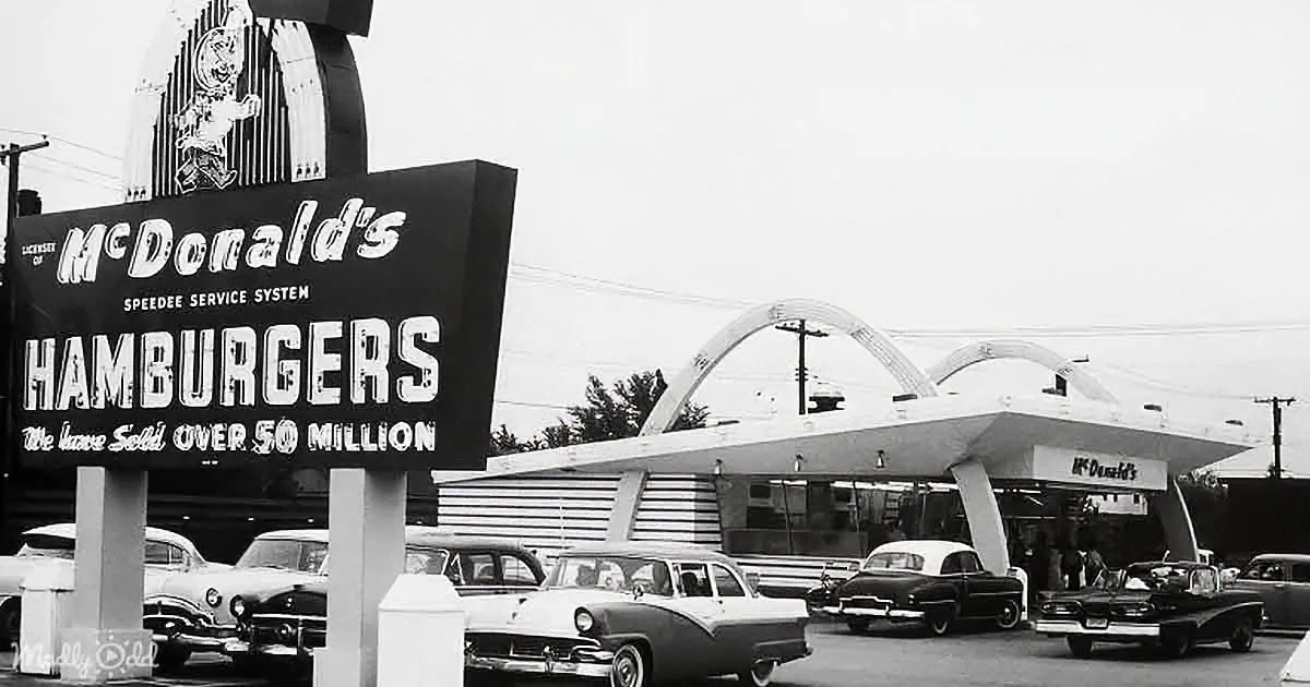 A vintage McDonald's sign advertises hamburgers with a "50 million sold" claim, set against classic cars and iconic arches.