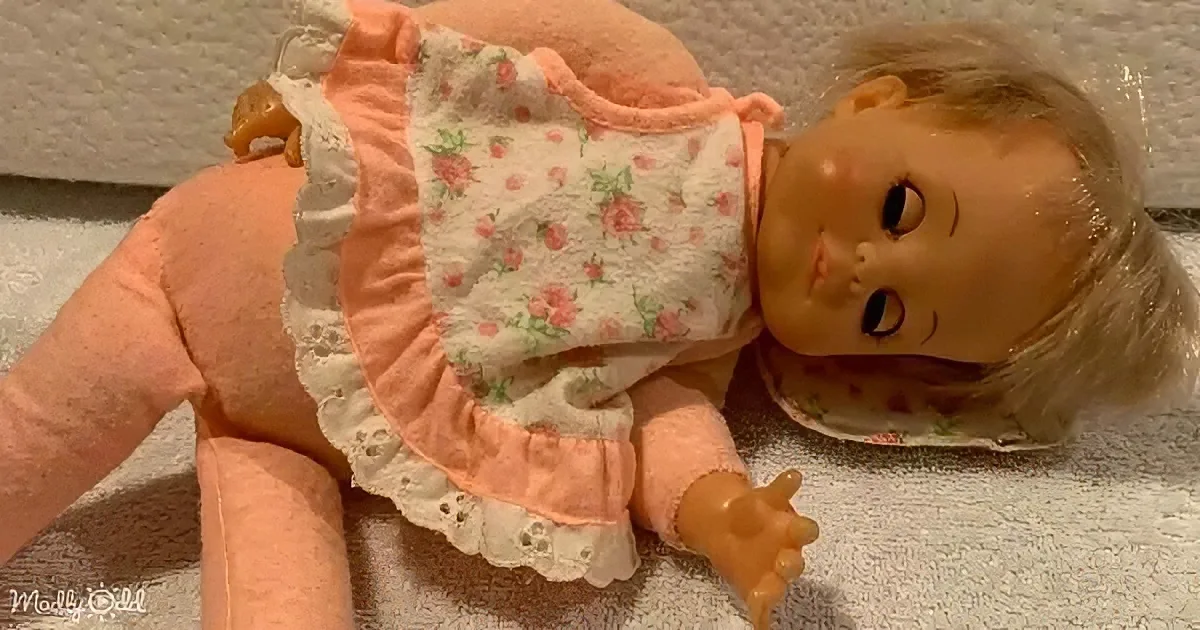 A doll with blonde hair and a peach dress lies on a textured surface.