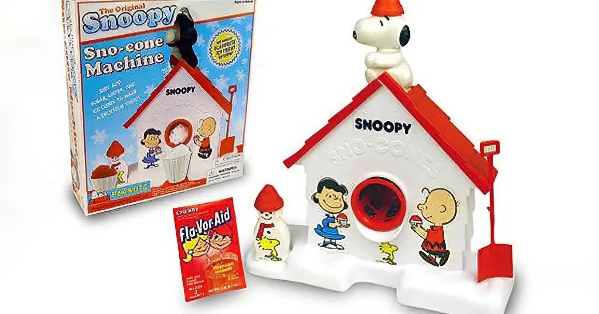 A Snoopy Sno-cone machine with a red roof, surrounded by Peanuts characters and a flavor packet.