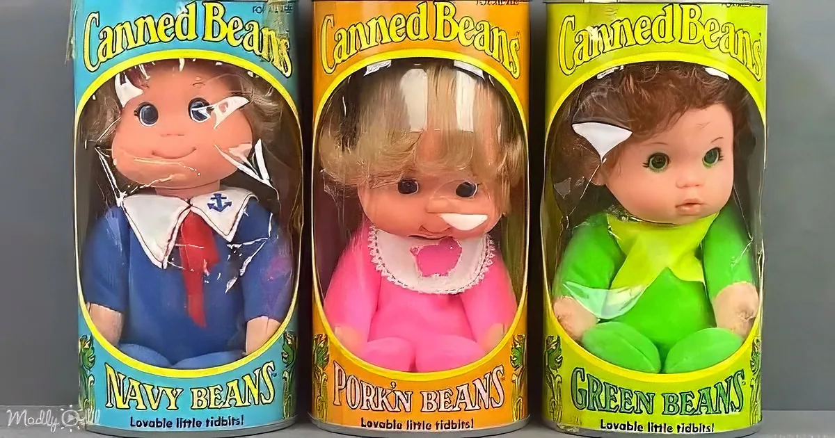 Three vintage dolls in cans labeled "Navy Beans," "Pork 'N Beans," and "Green Beans" are displayed.