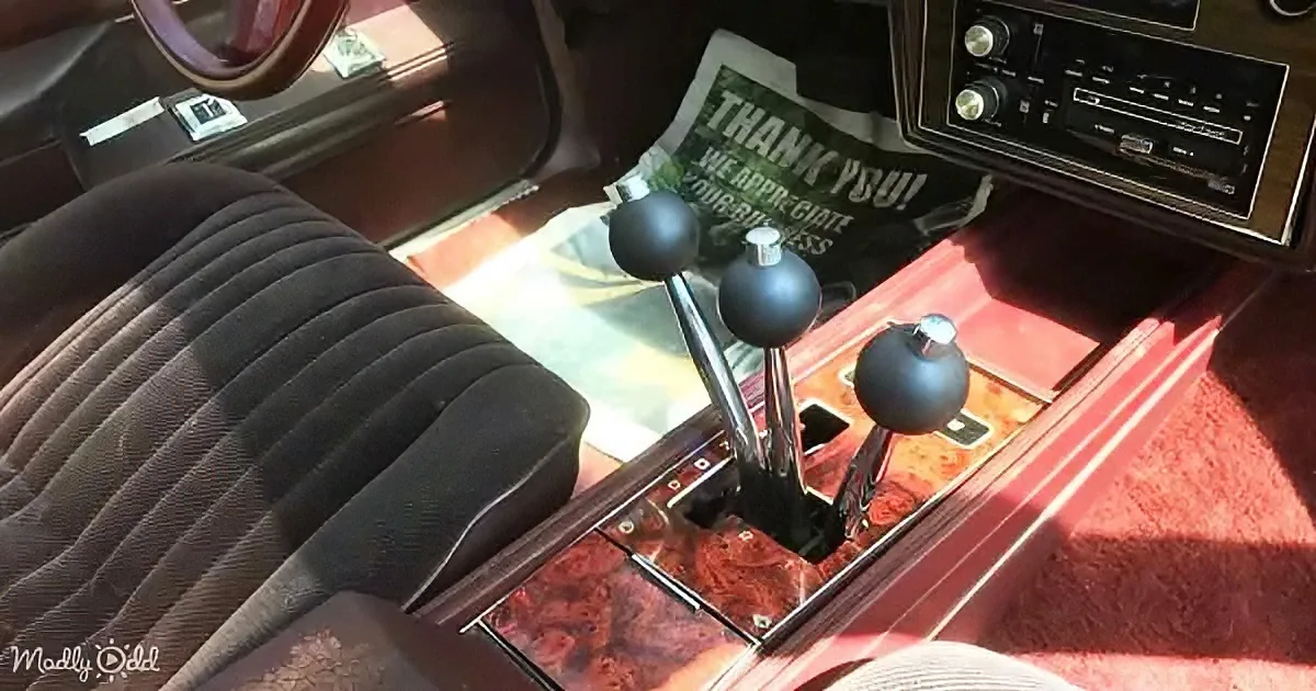 A vintage car interior with a three-speed manual transmission, red carpet, and retro dashboard.