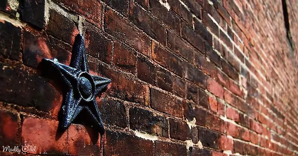 A black star-shaped object is affixed to a weathered red brick wall.