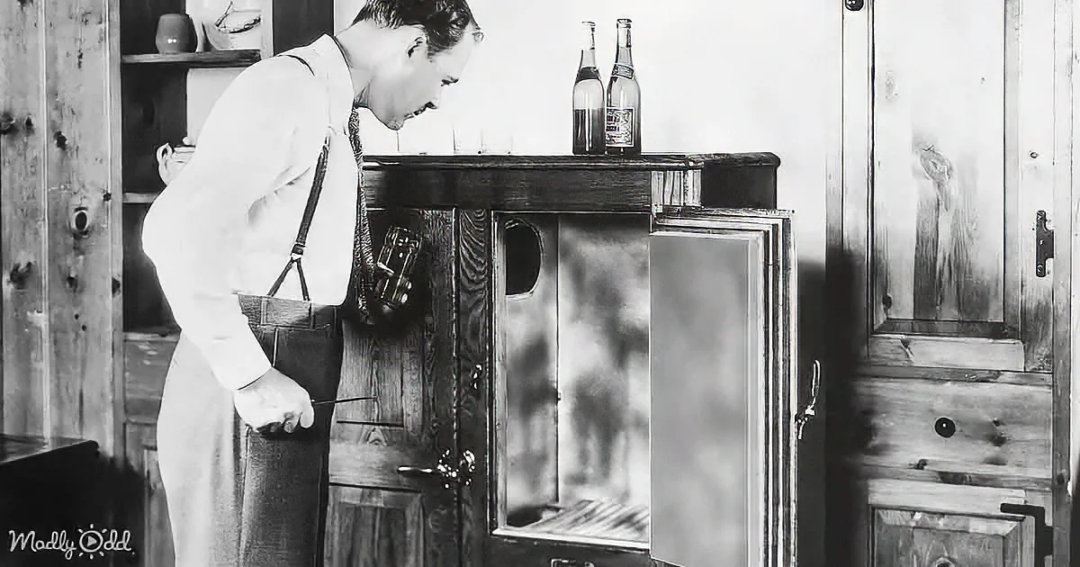 A man in suspenders stands beside a wooden cabinet, holding a bottle, with two bottles on top.