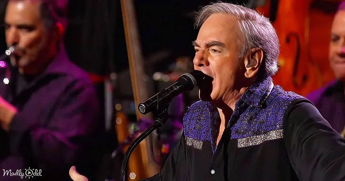 A man in a purple shirt sings into a microphone, with another musician in the background.