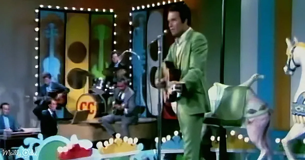 Elvis Presley in a green suit performs on stage with a band and colorful backdrop.