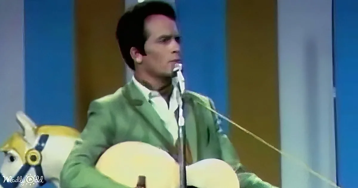 A man in a green suit plays a guitar on stage with a microphone and a yellow horse decoration.