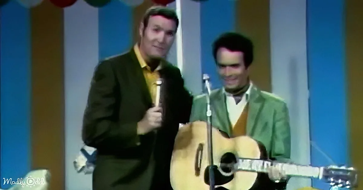 Two men in green suits perform on stage, one holding a microphone, the other playing guitar.