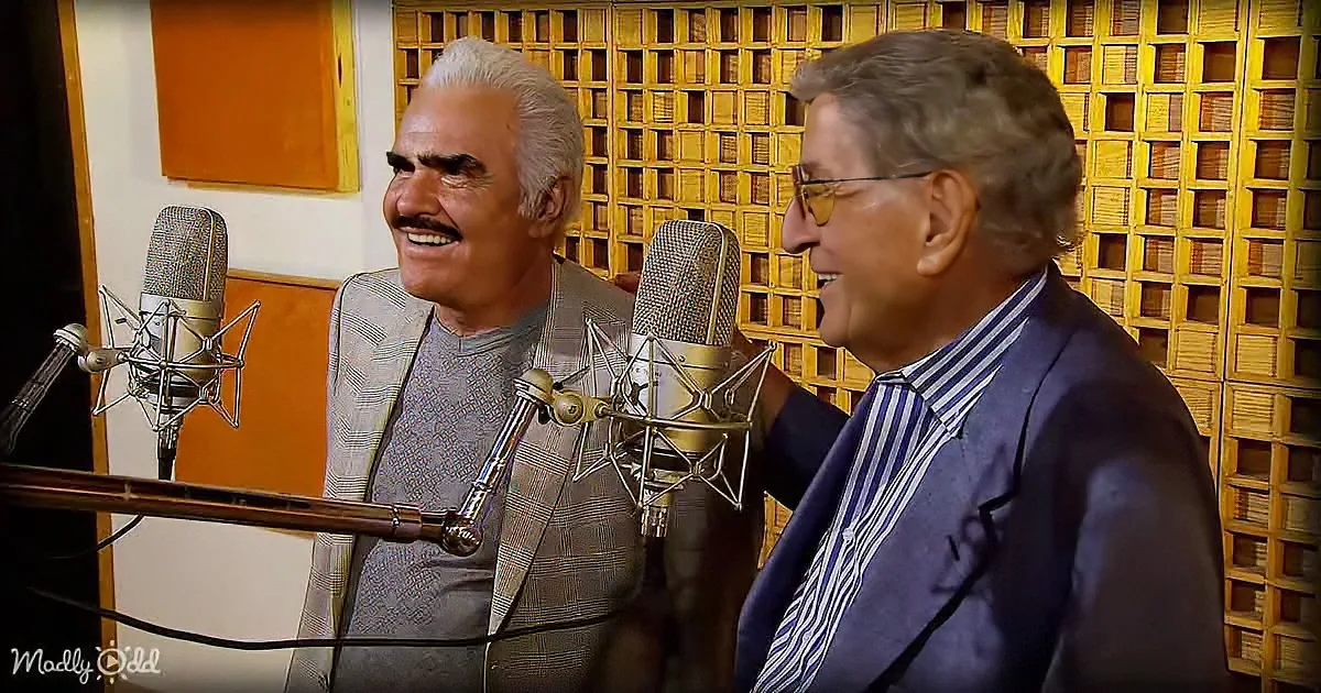 Two men in a recording studio, smiling, with microphones in front of them.