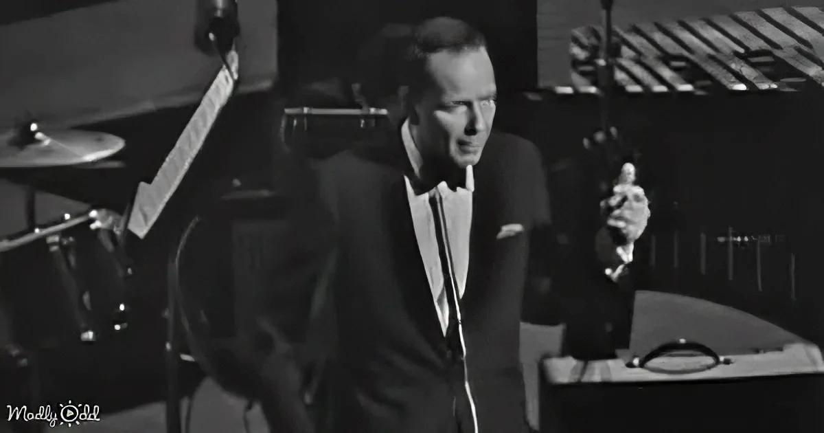 A man in a suit sings into a microphone, surrounded by musical instruments in a recording studio.