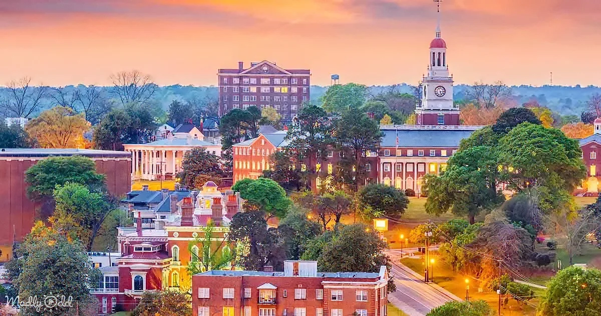 A picturesque sunset illuminates a historic campus with red brick buildings and a prominent clock tower.
