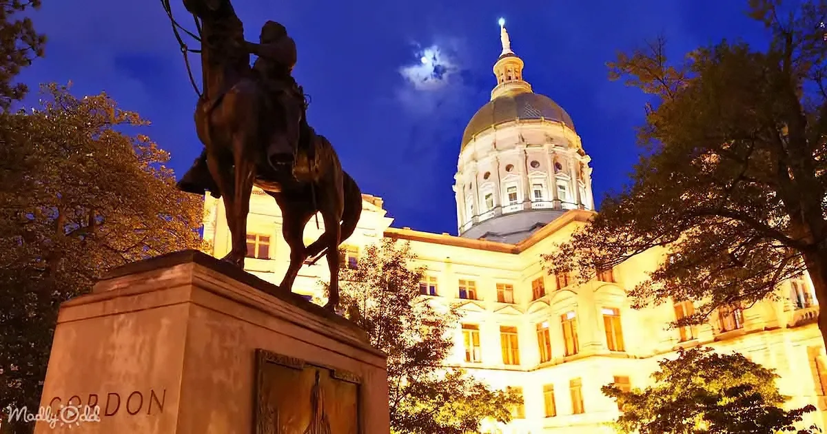 A statue of a man on horseback stands in front of a lit-up building with a golden dome, under a night sky.
