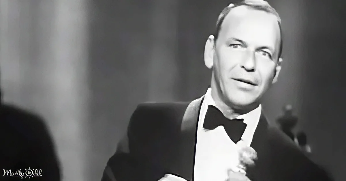 Frank Sinatra in a tuxedo, holding a microphone, looking to the side, with a blurred background.