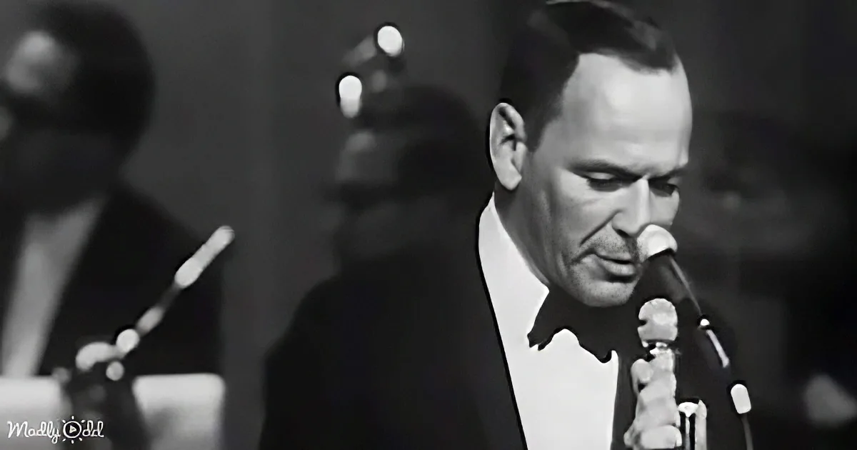 A man in a suit sings into a microphone, with a blurred background and another musician.