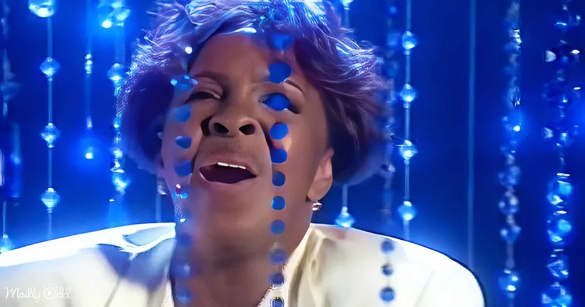 A person with short hair, wearing a white shirt, is surrounded by blue lights and sparkles.