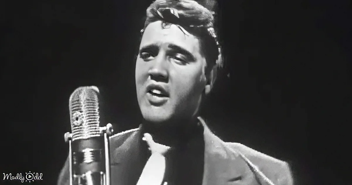 Elvis Presley sings into a microphone, wearing a suit and tie, against a dark background.