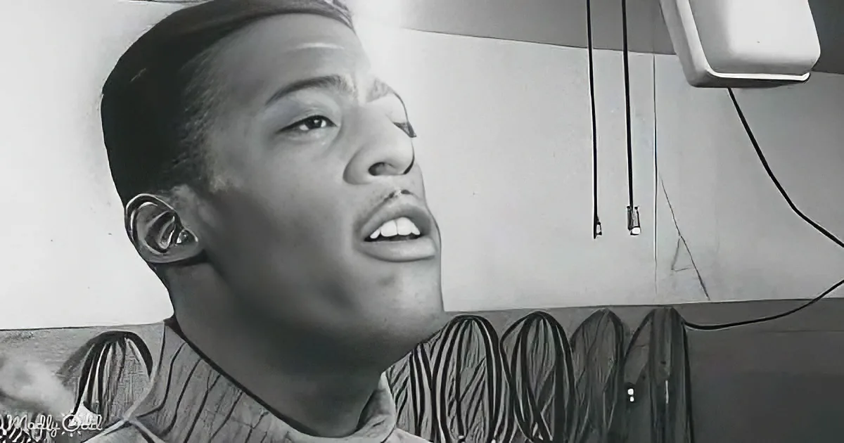 A person with a hat on, looking up, with a black-and-white background showing a ceiling and hanging wires.