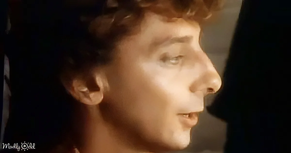 A person with curly hair, wearing a dark shirt, is shown in profile with a light source illuminating their face.
