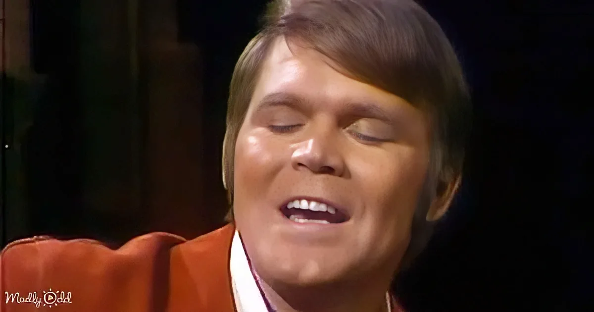 A person with short hair, wearing a red suit, is singing with eyes closed.