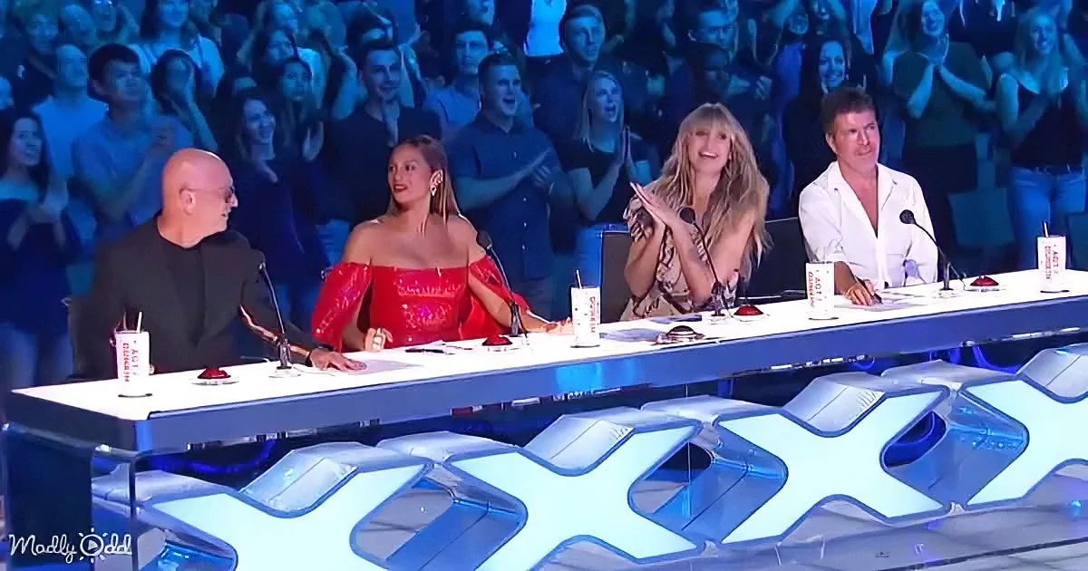 Judges on a panel with a large audience clapping behind them.