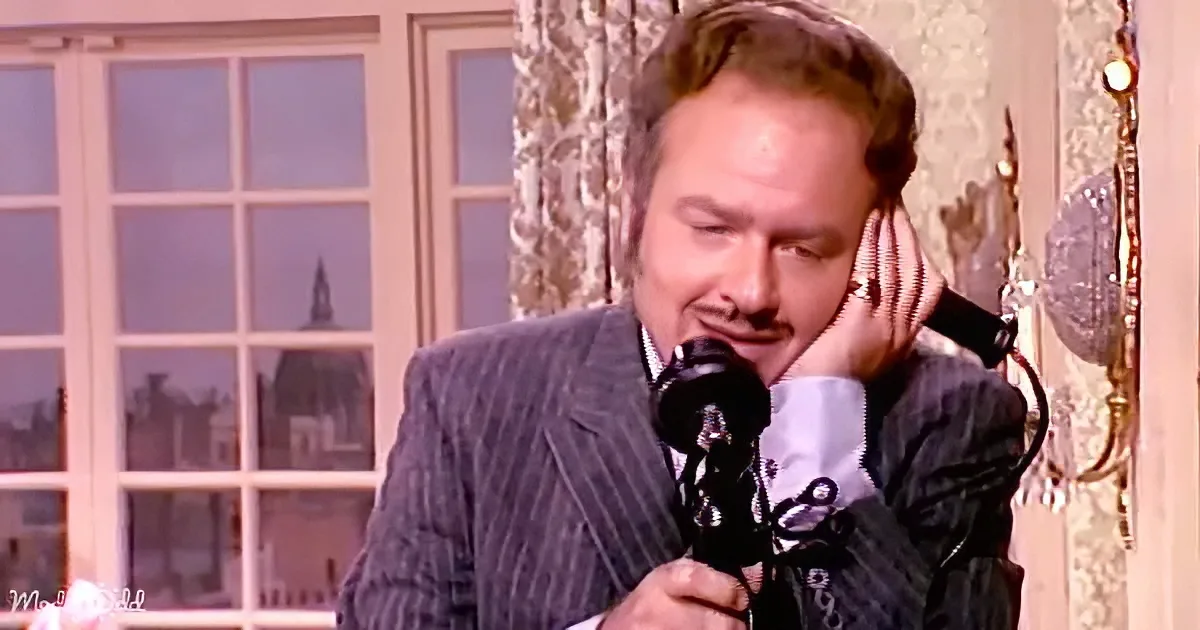 A man in a suit holds a vintage telephone to his ear, appearing to listen intently.