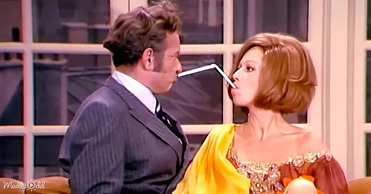 A man in a suit and a woman in a yellow dress are sharing a drink from a straw.
