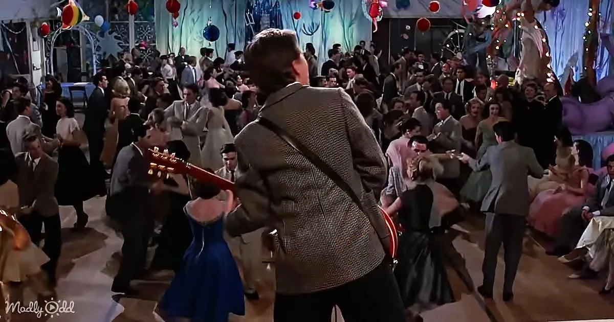 A man in a suit plays guitar amidst a lively dance floor filled with people in formal attire.