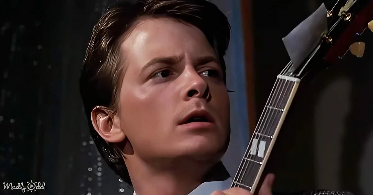 A person holding a guitar, looking up with a focused expression, in a dimly lit setting.