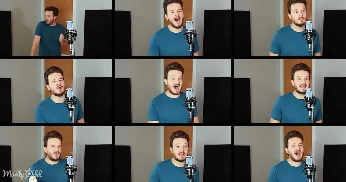 A man in a blue shirt sings into a microphone in a studio setting with black acoustic panels.