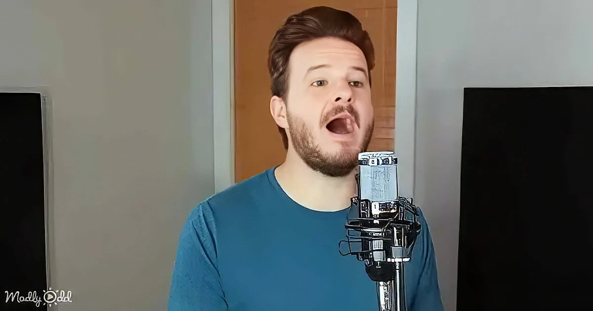 A man in a teal shirt sings into a microphone in a room with a door and wall.