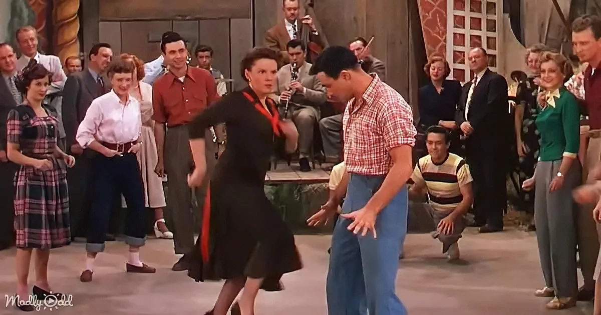 A man and woman dance in a lively scene, surrounded by onlookers and musicians.