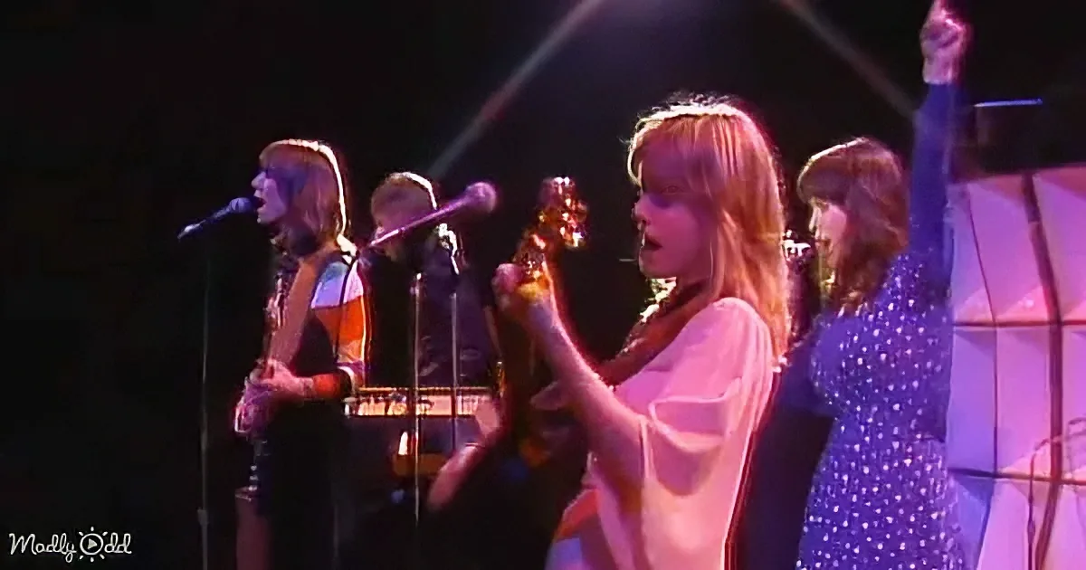 A woman in a white shirt sings passionately on stage with a band.