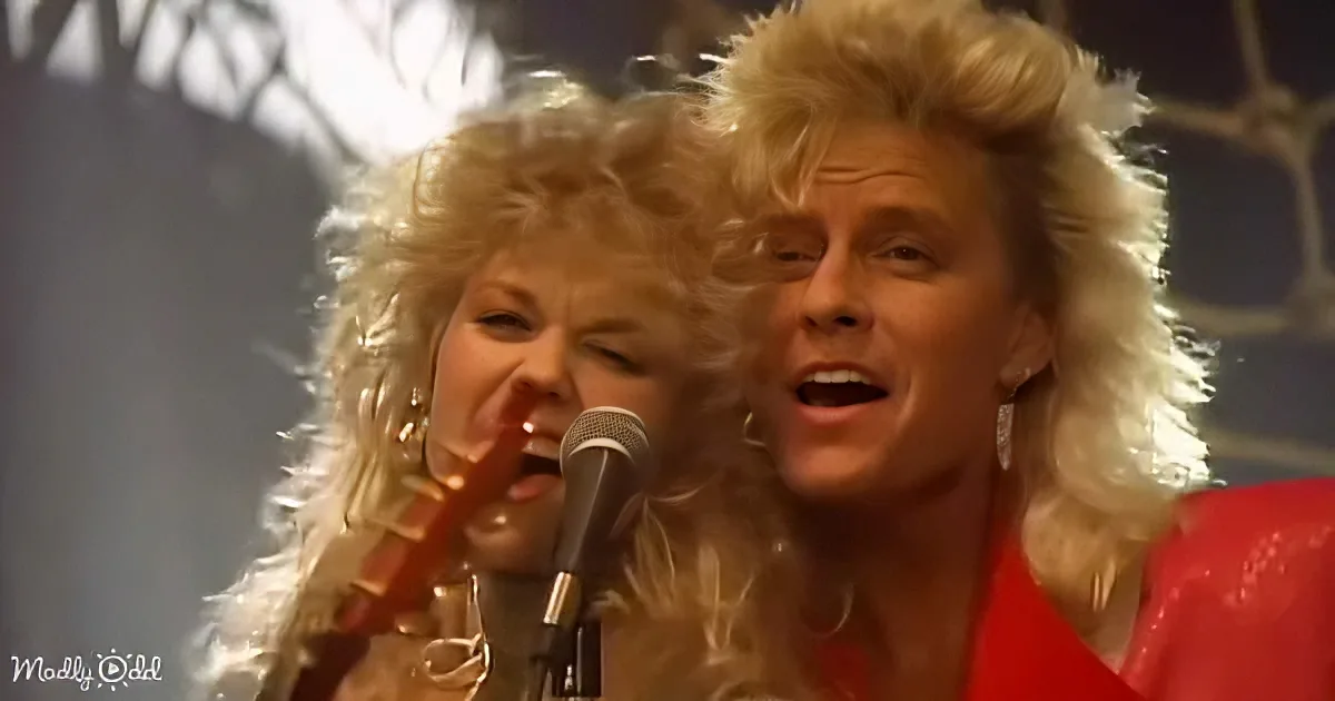 A man and woman with voluminous blonde hair sing passionately into a microphone.