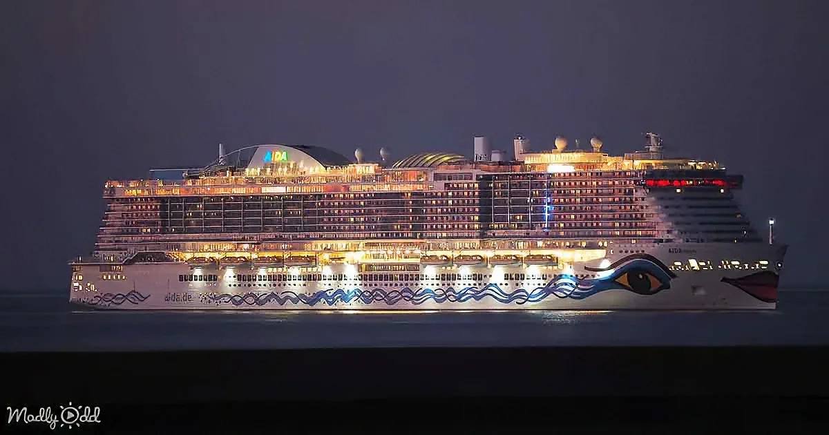 A large, brightly lit cruise ship with a colorful eye design on its side is docked at night.