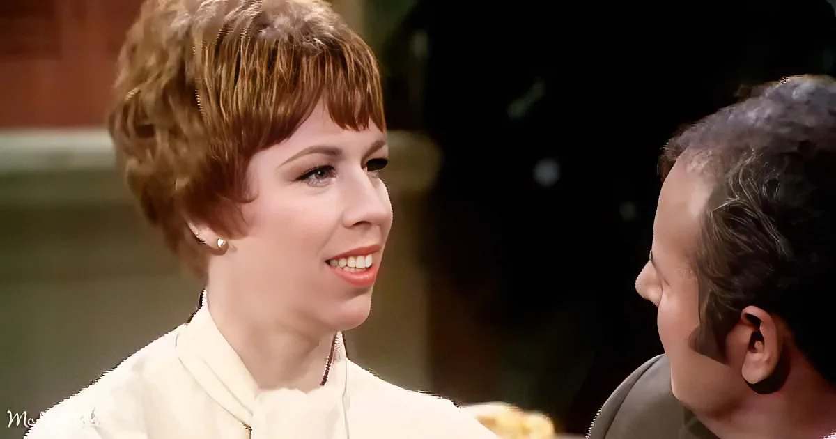A woman with short, styled hair and a white outfit smiles while looking at a man with dark hair.