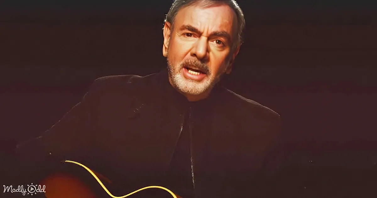A man in a black jacket holds a guitar, singing with a dark background.