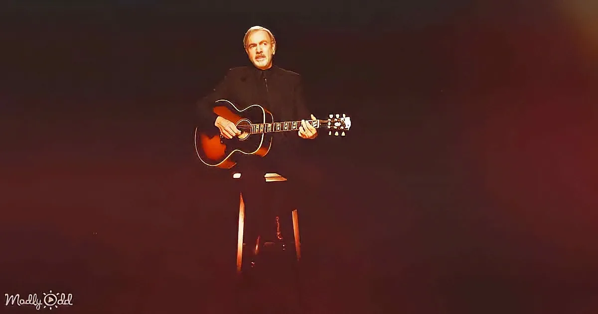 A man in black plays an acoustic guitar on stage, bathed in red light.